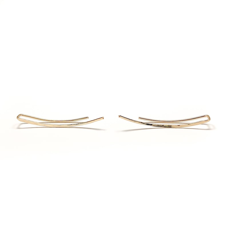 May include: A pair of gold ear cuffs. The cuffs are made of thin, hammered metal and have a simple, curved design.