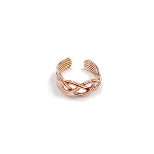 May include: A rose gold-colored toe ring with a braided design. The ring features an open design, with the braided section in the center and multiple parallel bands forming the open ends. The ring is set against a white background.