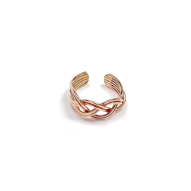 May include: A rose gold-colored toe ring with a braided design. The ring features an open design, with the braided section in the center and multiple parallel bands forming the open ends. The ring is set against a white background.