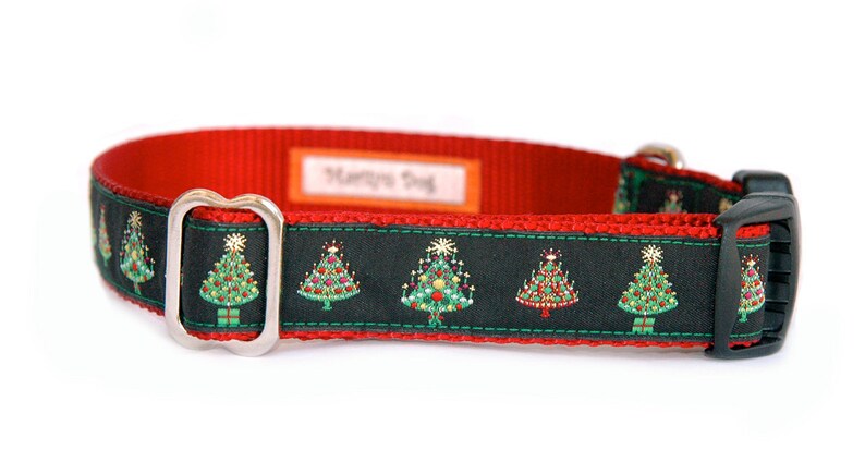 May include: A red and black dog collar with a silver buckle. The collar has a green and red Christmas tree pattern with gold accents. The collar has the words 'Happy Dog' printed on the red portion of the collar.