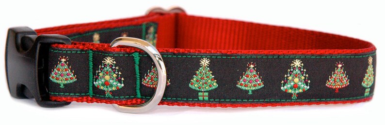 May include: A red and black dog collar with a silver D-ring and a black plastic buckle. The collar has a repeating pattern of green Christmas trees with red and gold ornaments on a black background.