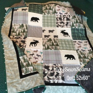 May include: A patchwork quilt featuring forest and wildlife designs. The quilt has squares with bears, moose, and trees in shades of green, gray, and white. The quilt measures 52x60 inches.