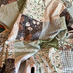 May include: A patchwork quilt featuring a variety of fabric squares in sage green, blush pink, and dark brown. The patterns include floral prints, a grey and white gingham check, and a textured olive green minky fabric. Text reads LoveSewnSeams.