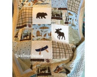 May include: A patchwork quilt with a woodland theme. The quilt features a brown bear, a moose, a canoe, and a plaid pattern. The quilt is made with a variety of fabrics, including flannel and cotton. The quilt is edged with a light blue trim. The quilt is perfect for a baby's nursery or a child's bedroom.