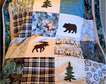Könnte beinhalten: Eine Patchwork-Decke mit Waldmotiv. Die Decke besteht aus verschiedenen Stoffen mit unterschiedlichen Mustern, darunter Karo, Bäume und Tiere. Die Decke ist beige, braun, blau und grün. Die Decke trägt den Text "Love Sewn Seams" in der linken unteren Ecke.