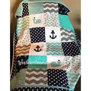 May include: A baby quilt with a nautical theme. The quilt is made of various fabrics in shades of blue, gray, and white. It features appliqued whales and anchors. The quilt is bordered with a turquoise trim. The text "Love Sewn Seams" is visible in the lower left corner.