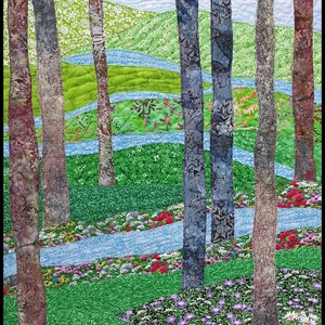 May include: A quilted fabric art piece depicting a forest scene with tall trees, winding blue streams, and a field of colorful flowers. The trees are brown, blue, and gray, and the flowers are red, pink, purple, and white.