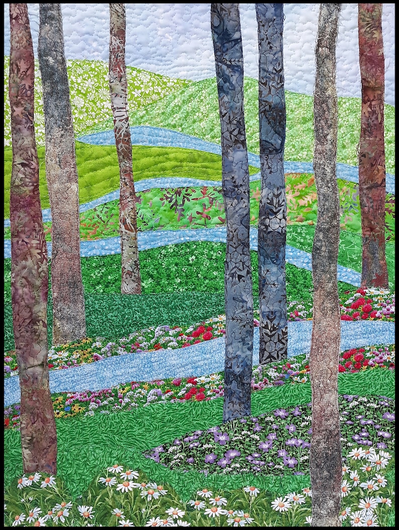 May include: A quilted fabric art piece depicting a forest scene with tall trees, winding blue streams, and a field of colorful flowers. The trees are brown, blue, and gray, and the flowers are red, pink, purple, and white.