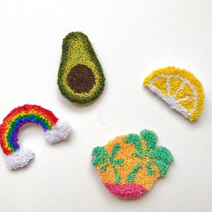 Puede incluir: Colección de parches bordados coloridos. Los parches incluyen un arcoíris con nubes blancas, un aguacate verde con un hueso marrón, una rodaja de limón amarilla y una fruta rosa, naranja y verde. Estos parches son probablemente para ropa o accesorios.