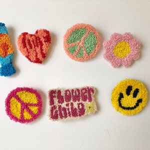 Puede incluir: Una colección de parches coloridos y texturizados con un tema retro. Los diseños incluyen una lámpara de lava, un corazón, símbolos de la paz, una flor, una carita sonriente y las palabras "Flower Child". Los parches están hechos con una técnica de hilo en bucle.