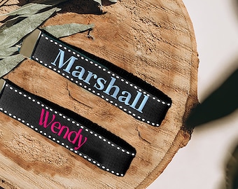 May include: Two black keychains with white stitching. The top keychain has the name "Marshall" embroidered in light blue. The bottom keychain has the name "Wendy" embroidered in pink.