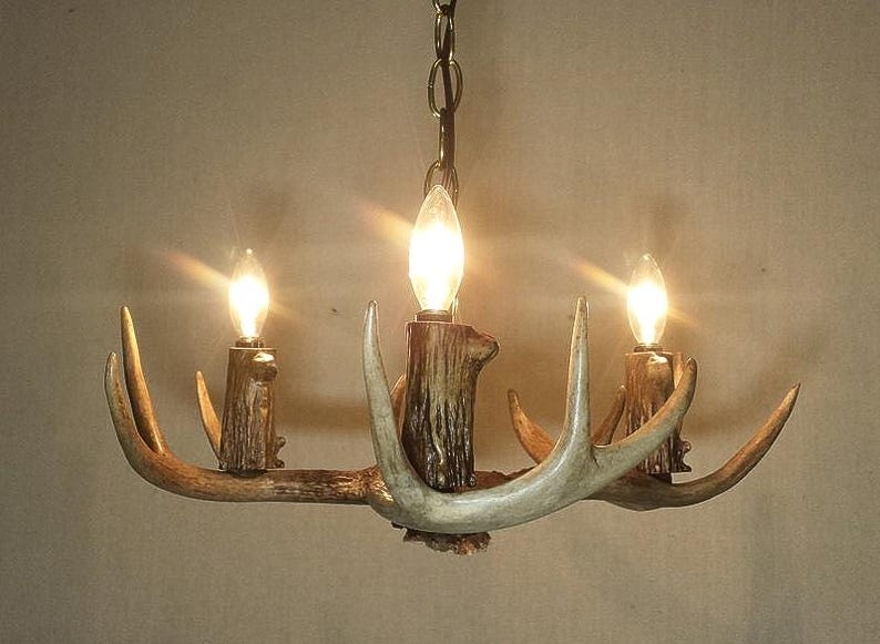 May include: A chandelier made from antlers with three light bulbs. The antlers are a natural light brown colour and the bulbs are clear glass.