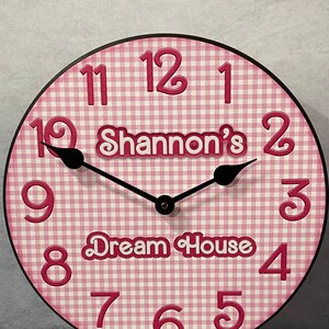 May include: Pink and white gingham clock with black hands and a black stand. The clock face has the numbers 1-12, the words "Shannon's Dream House" and a black clock hand.