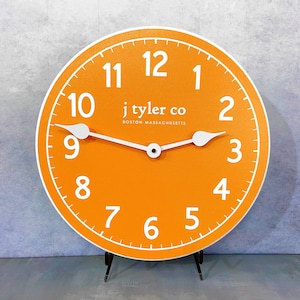 May include: Orange clock face with white numbers and hands. The clock face reads "j tyler co BOSTON MASSACHUSETTS".