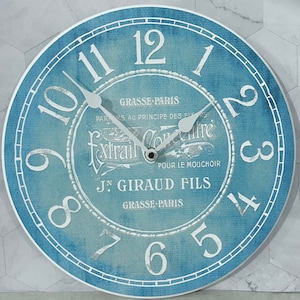 May include: A blue and white round clock with Roman numerals and the text "GRASSE-PARIS" and "J.N. GIRAUD FILS" in a decorative font.