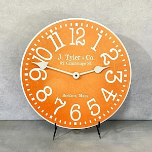May include: Orange clock face with white numbers and hands. The clock face has the text "J. Tyler & Co. 82 Cambridge St. Boston, Mass."