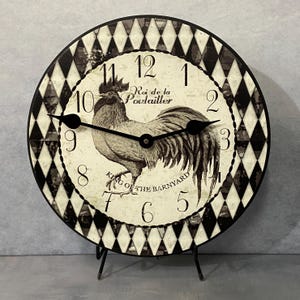 May include: A black and white rooster clock with a diamond pattern background. The clock face reads "Roi de la Poulailler" and "King of the Barnyard".