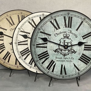 May include: Three decorative wall clocks with Roman numeral faces. The clocks have a distressed, vintage look. The clock faces are white, beige, and blue. The blue clock face has the text "Chateau-Thierry" and "Joseph Tyler & Co. BOSTON MASS".