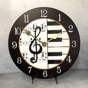 May include: A black and white clock with a treble clef and piano keys design. The clock face has black numbers on a white background. The clock is on a black stand.