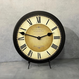 May include: Black and cream colored clock with Roman numeral markings. The clock face has the text "J. TYLER & CO. 82 Cambridge Street BOSTON MASS".