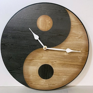 May include: A round wooden clock with a black and brown yin yang design. The clock has white hands and a gold center.