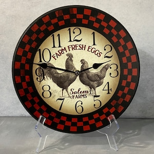 May include: A black and red checkered clock with a white face. The clock features a rooster and hen illustration with the text "Farm Fresh Eggs" and "Salem Farms".