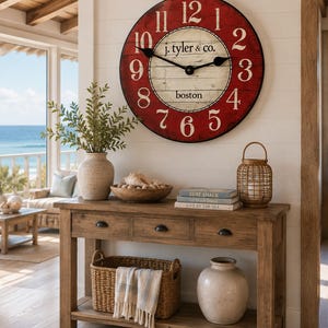 May include: A large round wall clock with a red outer ring featuring white numbers and a cream-colored center with black text reading j. tyler & co. and boston. The clock has black metal hands and a thin black frame, mounted on a white wall.