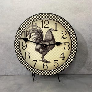 May include: A black and white rooster clock with a checkered border. The clock face has black numbers and hands. The rooster is in the center of the clock face.