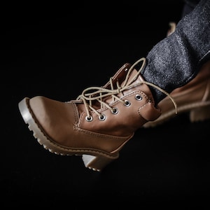May include: Brown leather lace-up boots with a thick sole. The boots are being worn by someone wearing jeans.