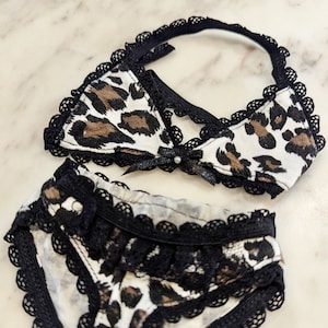 May include: A black and white leopard print lingerie set with black lace trim. The set includes a bra and matching underwear.