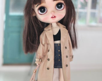 May include: A brown doll wearing a beige trench coat, a black top, a denim skirt, and black boots. The doll is holding a brown and black handbag.