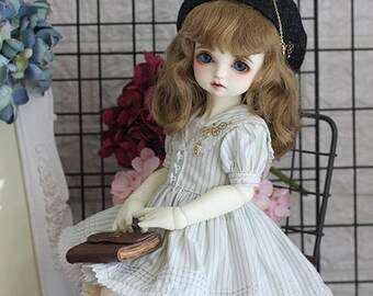 May include: A doll wearing a white and blue striped dress with a black beret, white knee-high socks, and black shoes. The doll is holding a brown book and sitting on a black metal chair.