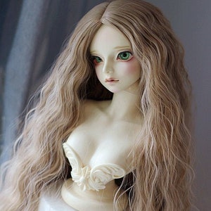 Puede incluir: Una cabeza de muñeca con cabello largo, ondulado y castaño claro. La muñeca tiene ojos verdes y lleva un busto esculpido blanco.