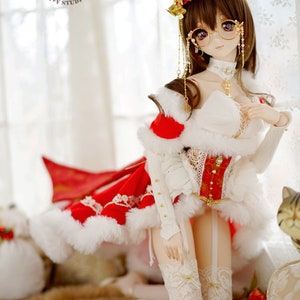 May include: A doll wearing a red and white Christmas dress with a white fur trim, a red hat with gold bells, and white lace stockings. The doll has brown hair and is wearing round glasses. The doll is sitting on a furry surface with a red rose in the background. +Merry Christmas+