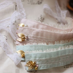 May include: Three layers of delicate lace fabric in pink, light blue, and white with gold accents and pearl embellishments. The fabric is soft and has a delicate, feminine feel. Cotton.