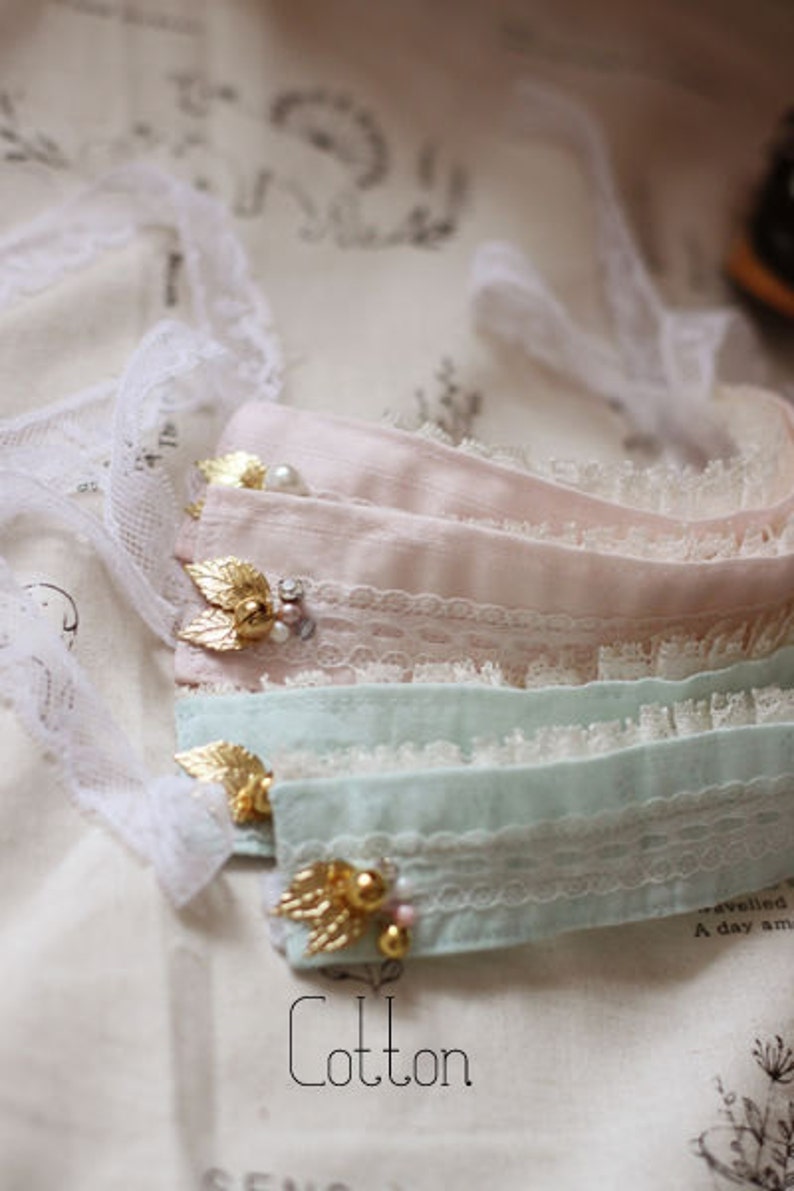 May include: Three layers of delicate lace fabric in pink, light blue, and white with gold accents and pearl embellishments. The fabric is soft and has a delicate, feminine feel. Cotton.