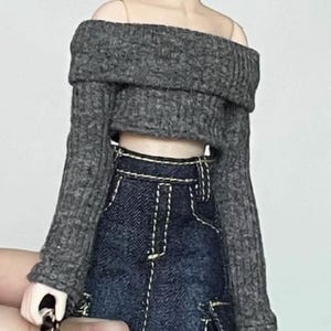 May include: A grey off-the-shoulder sweater with long sleeves and a cropped length. The sweater is made of a soft, knitted fabric.