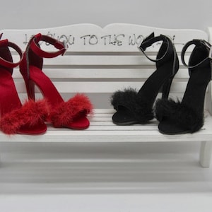 May include: Two pairs of high-heeled sandals with ankle straps and fluffy trim. One pair is red and the other is black. The sandals are sitting on a white bench.