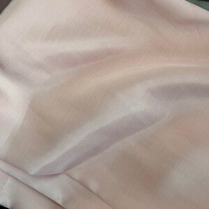 May include: A pale pink fabric with a smooth, silky texture. The fabric is folded and draped, showing its soft, flowing nature.
