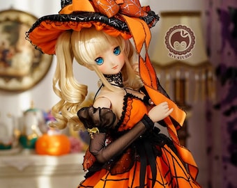 May include: A doll wearing a black and orange witch costume with a spiderweb pattern. The doll has blonde hair in pigtails and blue eyes. The costume includes a hat with a large orange bow and a spiderweb design, a black and orange dress with a spiderweb pattern, and black and orange tights.