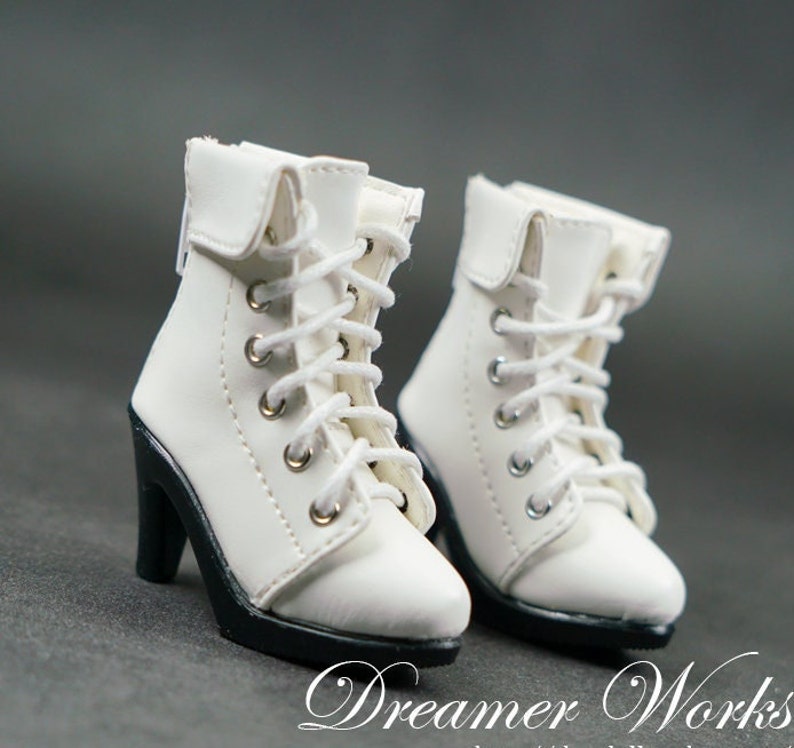 Puede incluir: Un par de botines blancos con cordones y tacones negros. Las botas tienen un estilo cl&aacute;sico y est&aacute;n hechas de un material liso similar al cuero.