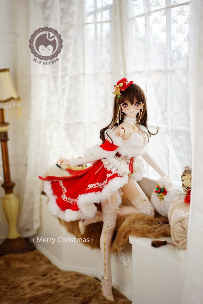 May include: A doll wearing a red and white Christmas dress with a white fur trim, a red hat, and gold glasses. The doll is holding a small bell and is sitting on a white windowsill with a furry rug.