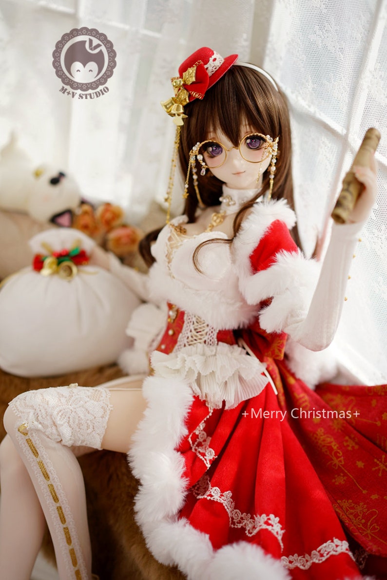 May include: A doll wearing a red and white Christmas dress with a white fur trim, a red hat with gold accents, and gold-rimmed glasses. The doll is holding a rolled-up scroll in one hand and has a white furry bag with gold accents next to her.