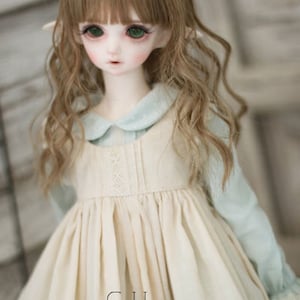 May include: A doll with long, wavy brown hair wearing a white dress with a blue collar and the word "Cotton" printed on the front.