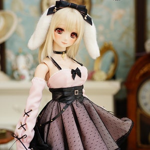 May include: A doll wearing a pink and black dress with a black belt and white bunny ears. The doll has blonde hair and blue eyes.