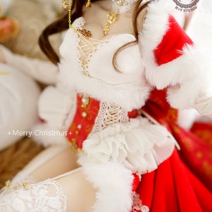 May include: A doll wearing a white and red Christmas outfit with a white fur trim. The doll has long brown hair, purple eyes, and is wearing a gold necklace and earrings. The doll is sitting on a white surface. +Merry Christmas+