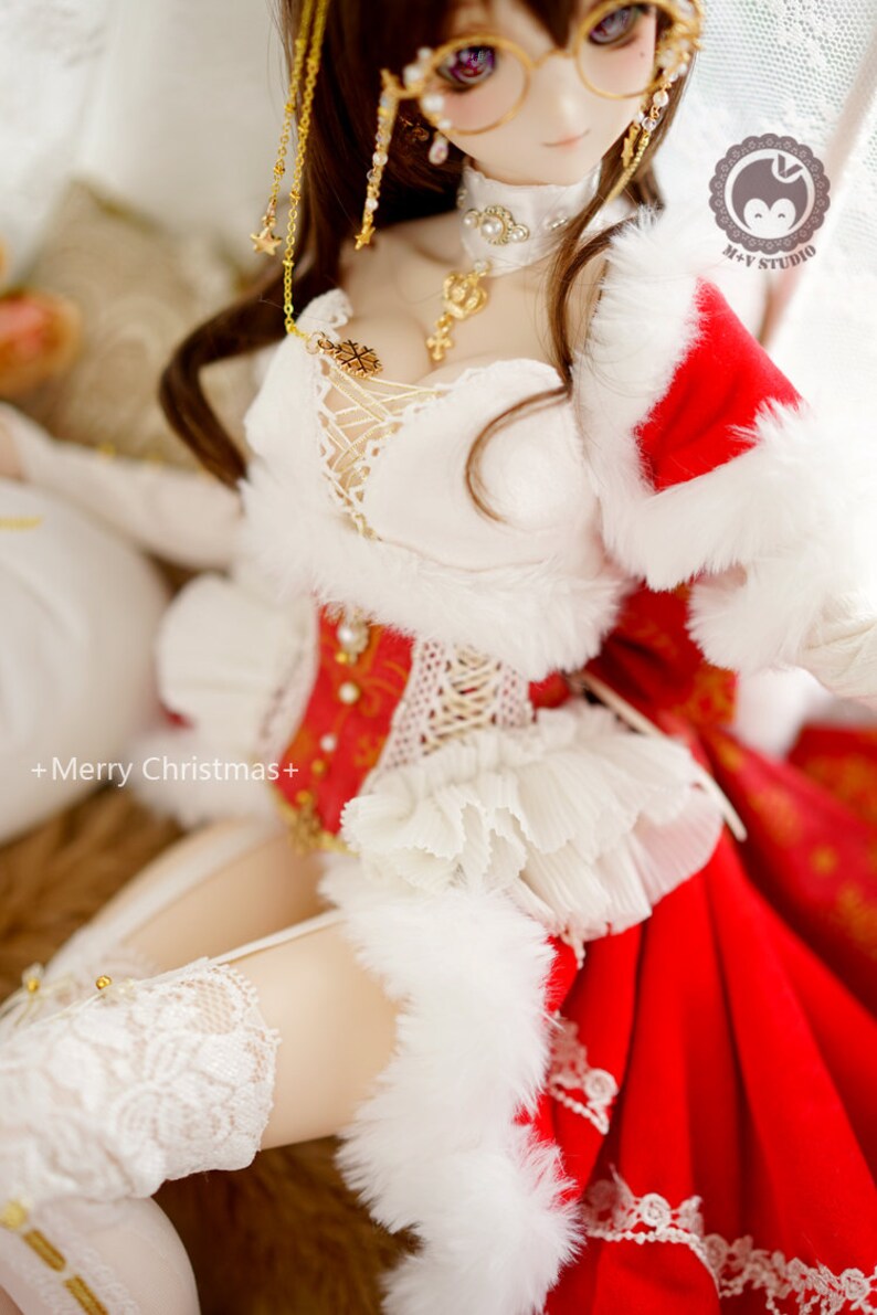May include: A doll wearing a white and red Christmas outfit with a white fur trim. The doll has long brown hair, purple eyes, and is wearing a gold necklace and earrings. The doll is sitting on a white surface. +Merry Christmas+