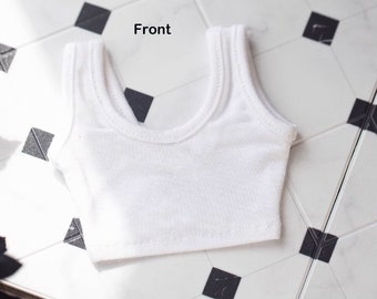 May include: White tank top with a scoop neck. The tank top is made of a soft, stretchy fabric and has a cropped fit.
