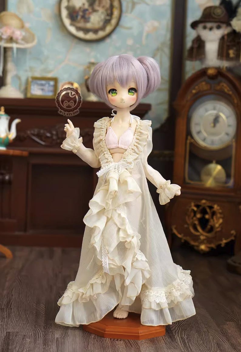 May include: A doll with lavender hair and green eyes, wearing a cream-colored ruffled robe and a pink bra. The doll is standing in a room with antique furniture and decor, including a grandfather clock and a fireplace.