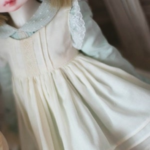 May include: A white dress with a lace trim and a green and white polka dot shirt underneath. The dress has a gathered skirt and a fitted bodice.
